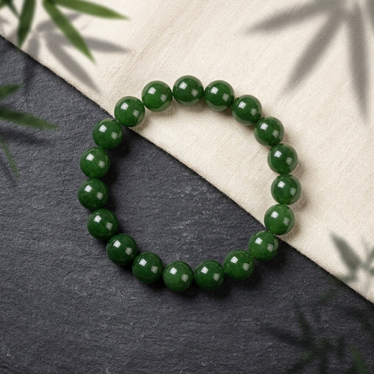 Bracelet perles de jadéite verte posé sur pierre noire et tissu de lin avec ombres de bambou. L'Atelier Wen.