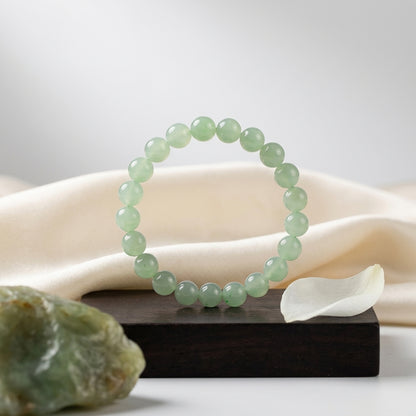 Bracelet d'aventurine sur socle en bois avec pierre brute et pétale blanc. Ambiance zen et naturelle.