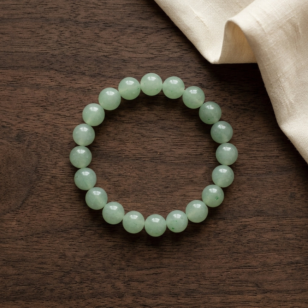Bracelet circulaire en perles d'aventurine naturelle posé sur bois sombre avec drapé de lin. L'Atelier Wen.